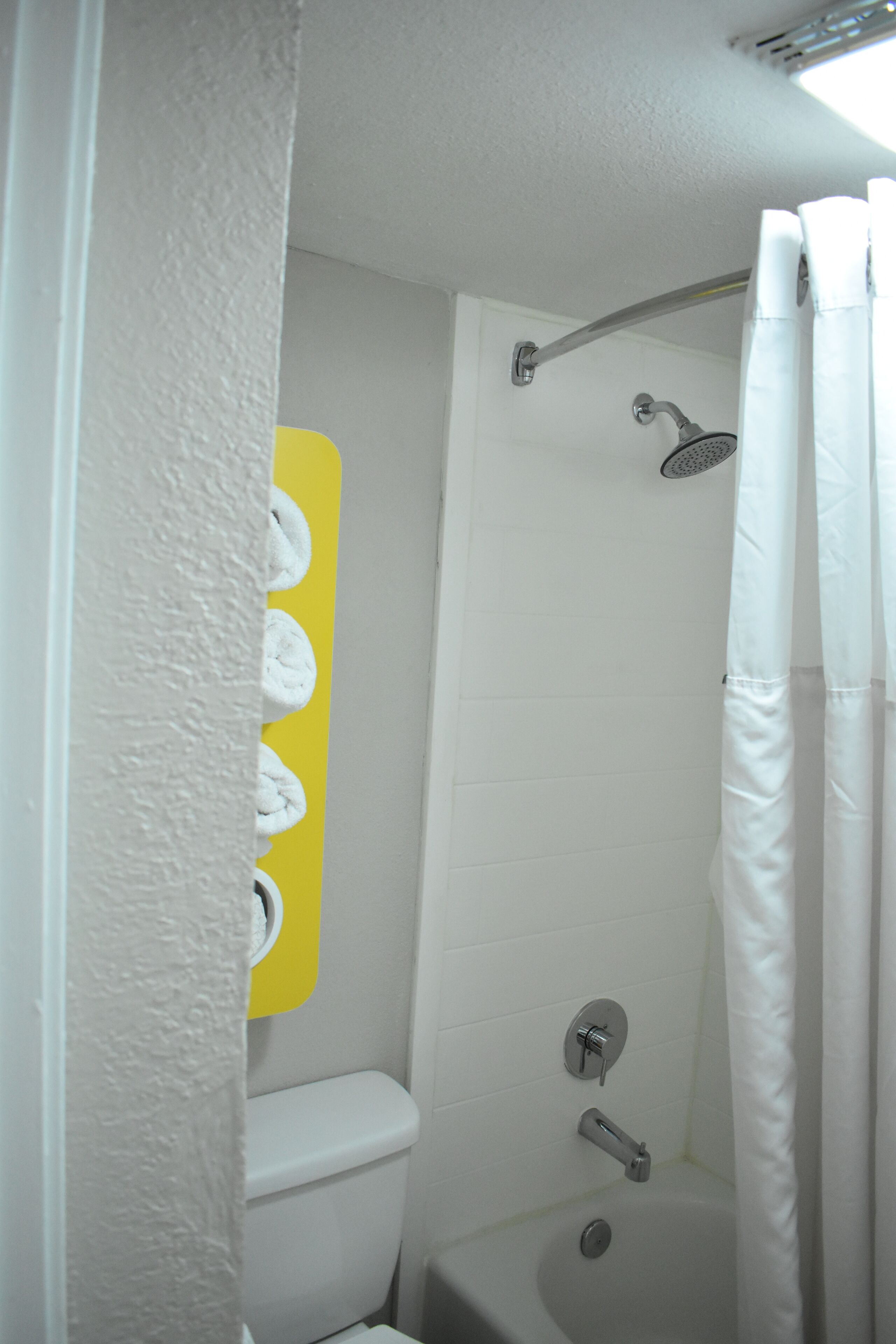 Ein Badezimmer mit einer weißen Badewanne, einer Duschbrause und einem gelben Handtuchhalter.