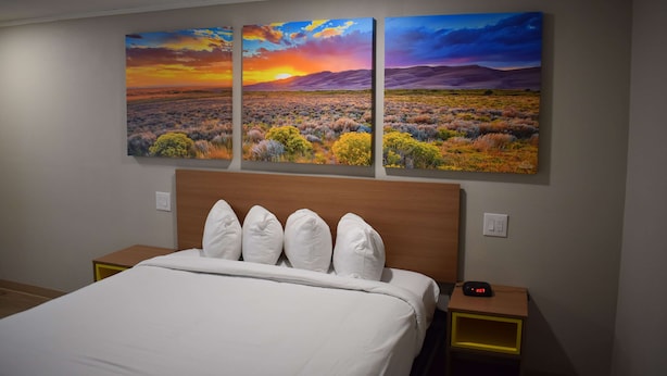 Habitación de hotel con una cama grande, cabecera de madera y tres cuadros colgados que representan un atardecer sobre un paisaje.