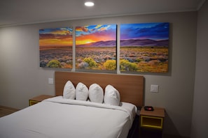 A hotel room with a large bed, a wooden headboard, and three wall-mounted paintings depicting a sunset over a landscape. - Days Inn by Wyndham San Antonio Alamo/Riverwalk (San Antonio)