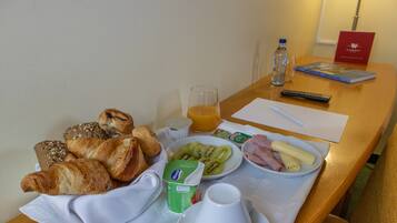 A breakfast table with croissants, a plate of fruit, a glass of orange juice, and a bottle of water.