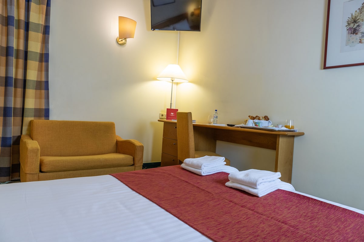 A hotel room with a bed, a sofa, a desk, and a lamp.