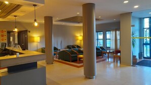 A hotel lobby with a reception desk, seating area, and large windows. - Flag Hotel Guimaraes Fafe (Fafe)