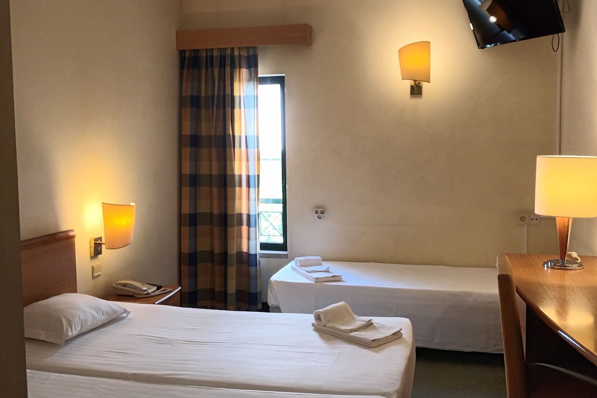 A hotel room with two beds, a desk, a television mounted on the wall, and a window with curtains.