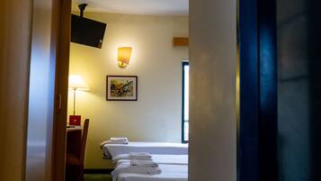 A hotel room with two beds, a desk with a chair, a TV mounted on the wall, and a painting.