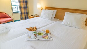 A neatly made bed with white linens, a tray of breakfast including croissants, fruits, and juice, and a red chair in the background. - Flag Hotel Guimaraes Fafe (Fafe)