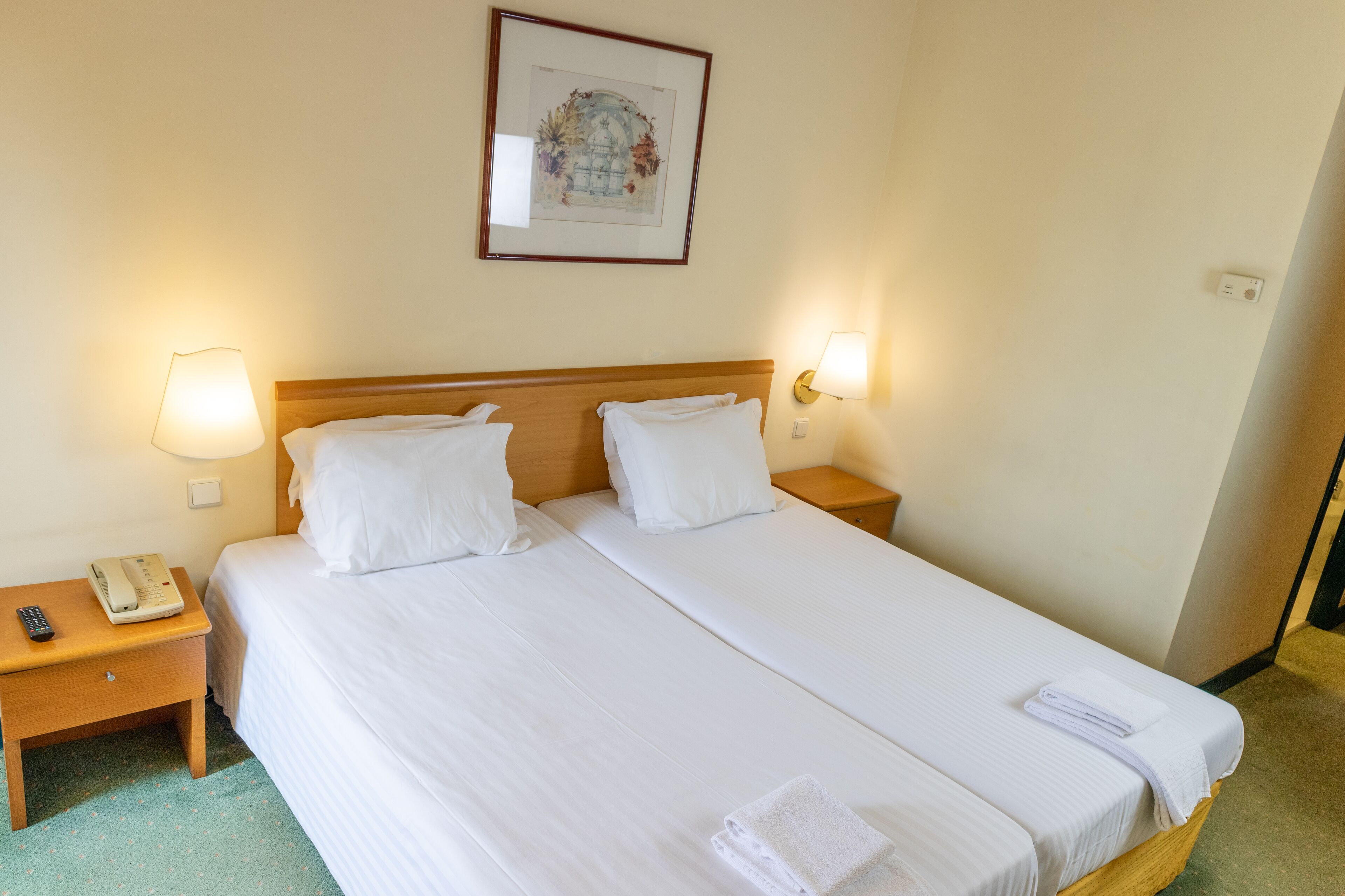 A double bed with white linens, two bedside tables, a framed picture on the wall, and a bedside lamp.