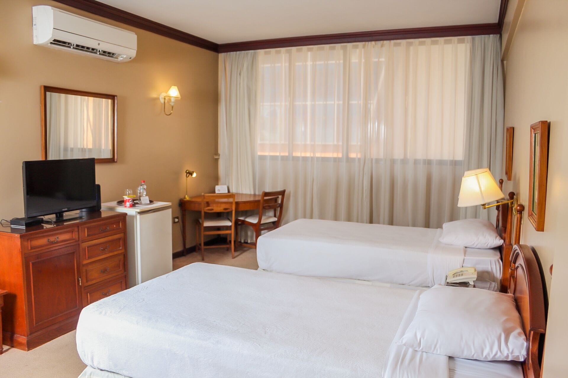 Een hotelkamer met twee bedden, een bureau met een televisie, een lamp en een telefoon.