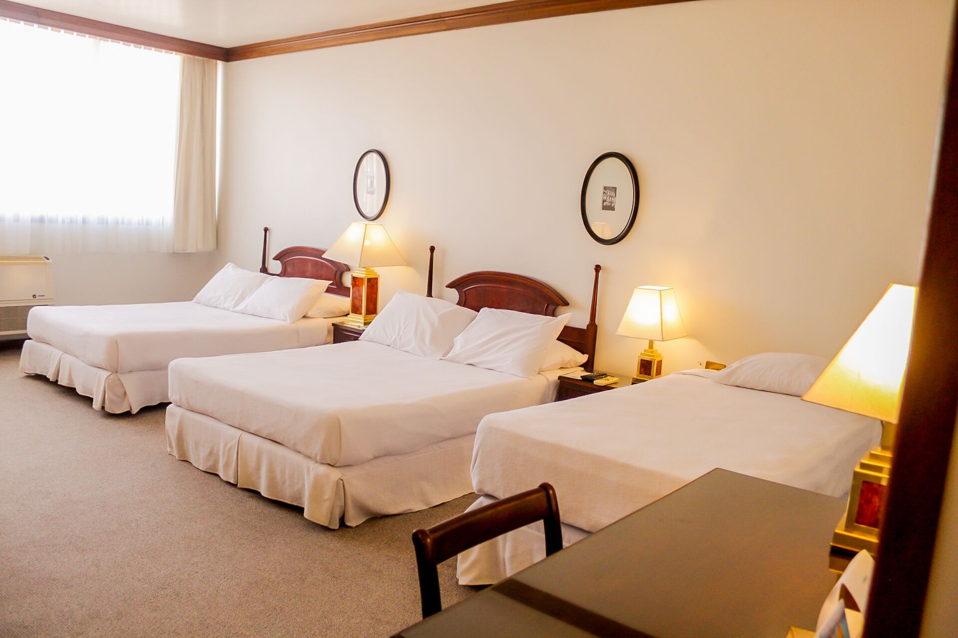 Une chambre d’hôtel avec deux lits, un bureau et une chaise. Il y a des tables de chevet avec des lampes et un miroir fixé au mur.