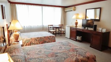 A hotel room with two beds, a desk with a chair, a television, and an air conditioning unit.