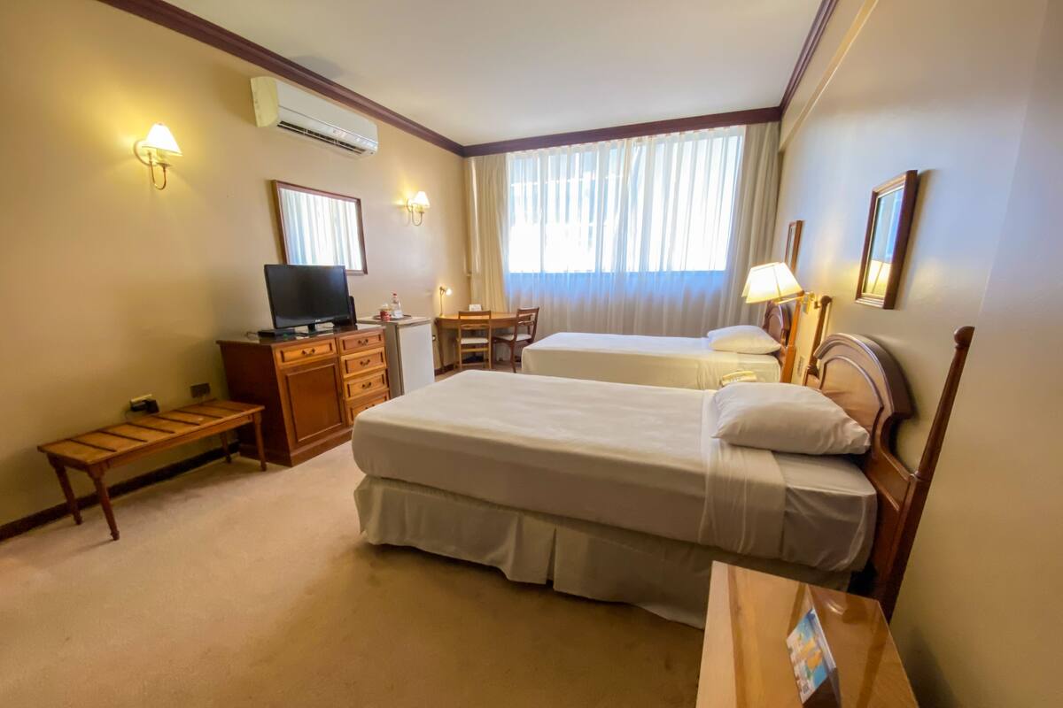 A hotel room with two beds, a desk, a television, and a small table.