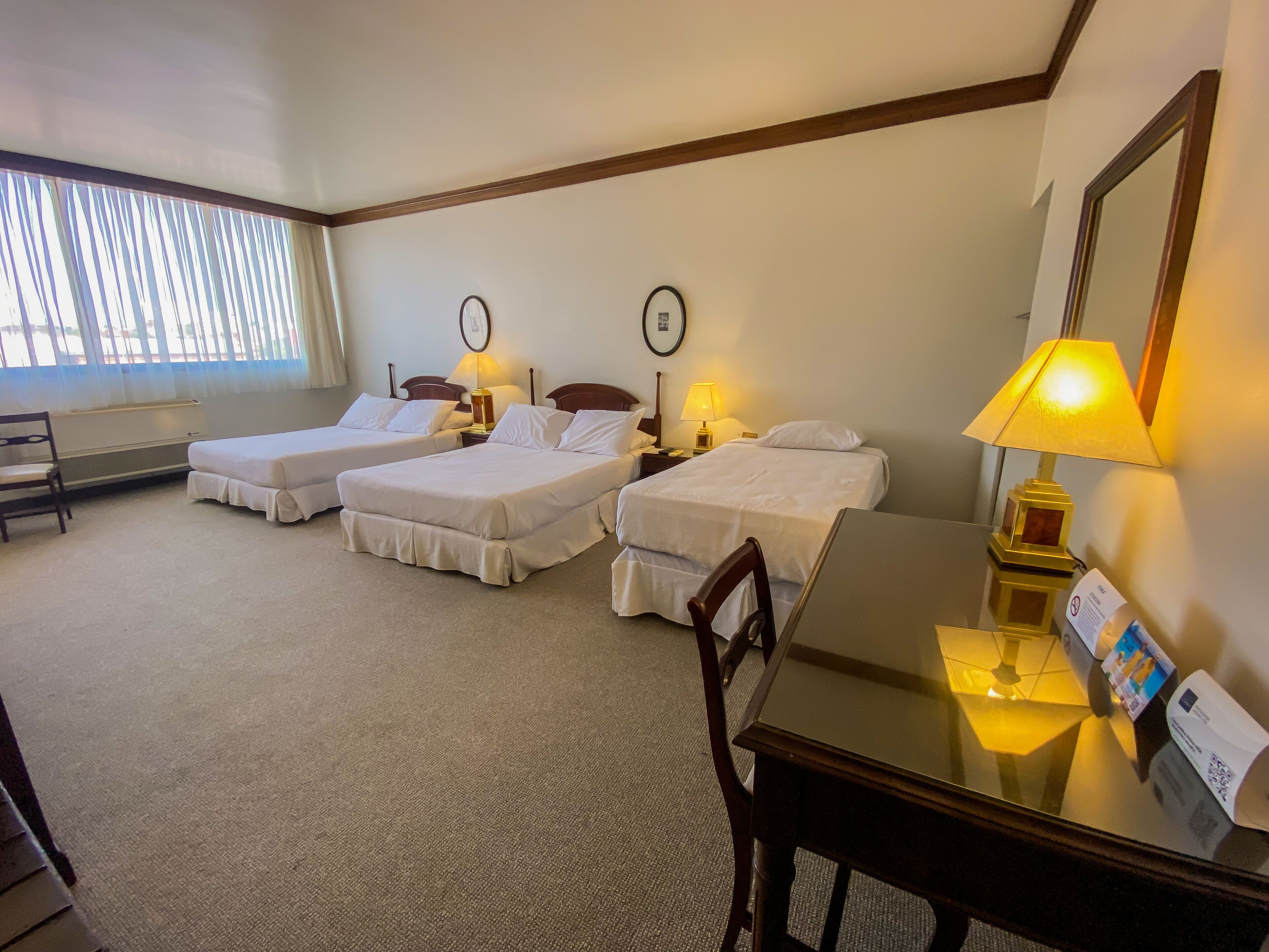 A hotel room with two single beds, a desk, a chair, and a window with blinds.