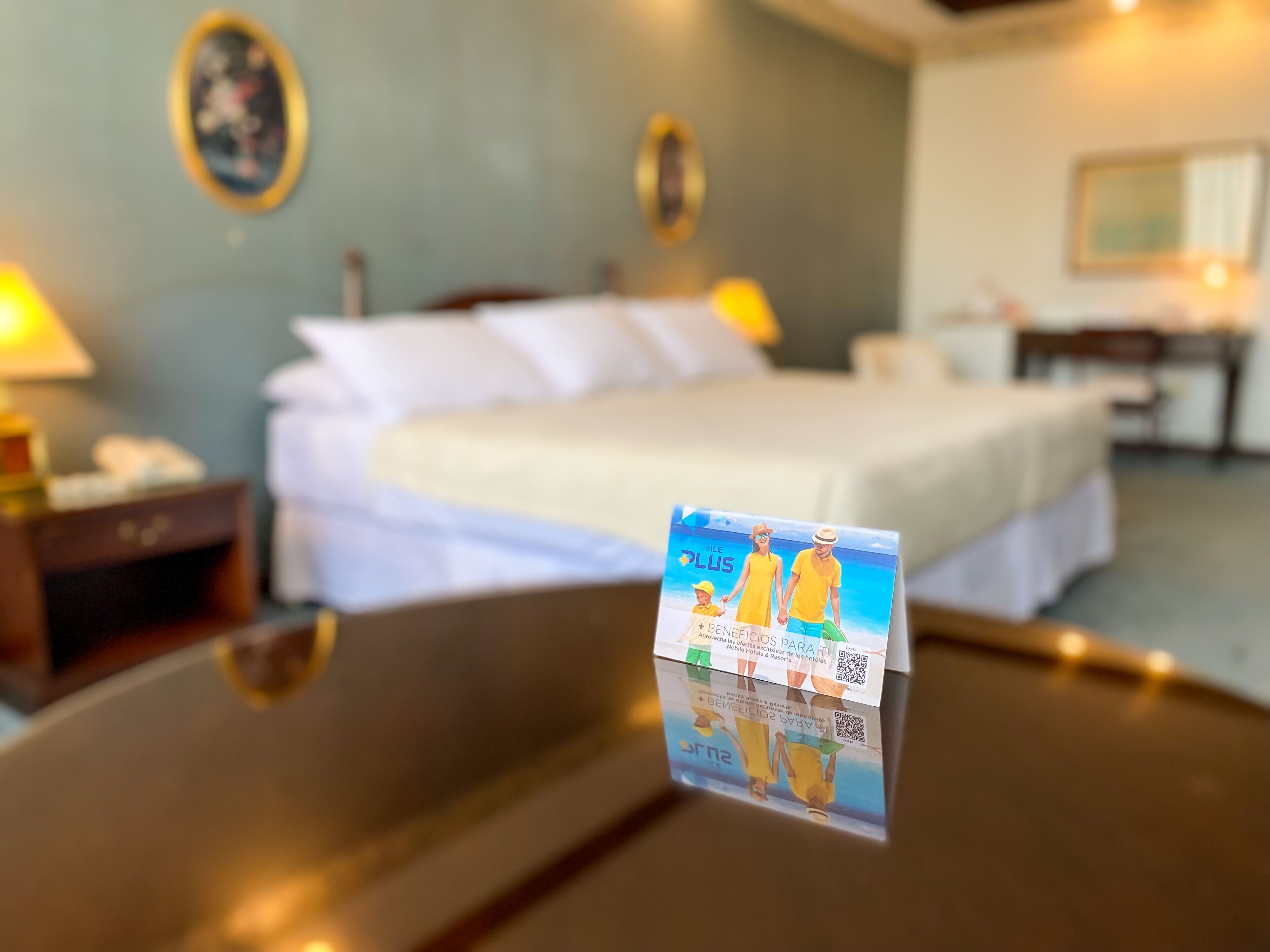 A hotel room with a bed, bedside table, lamp, and a framed picture on the wall.