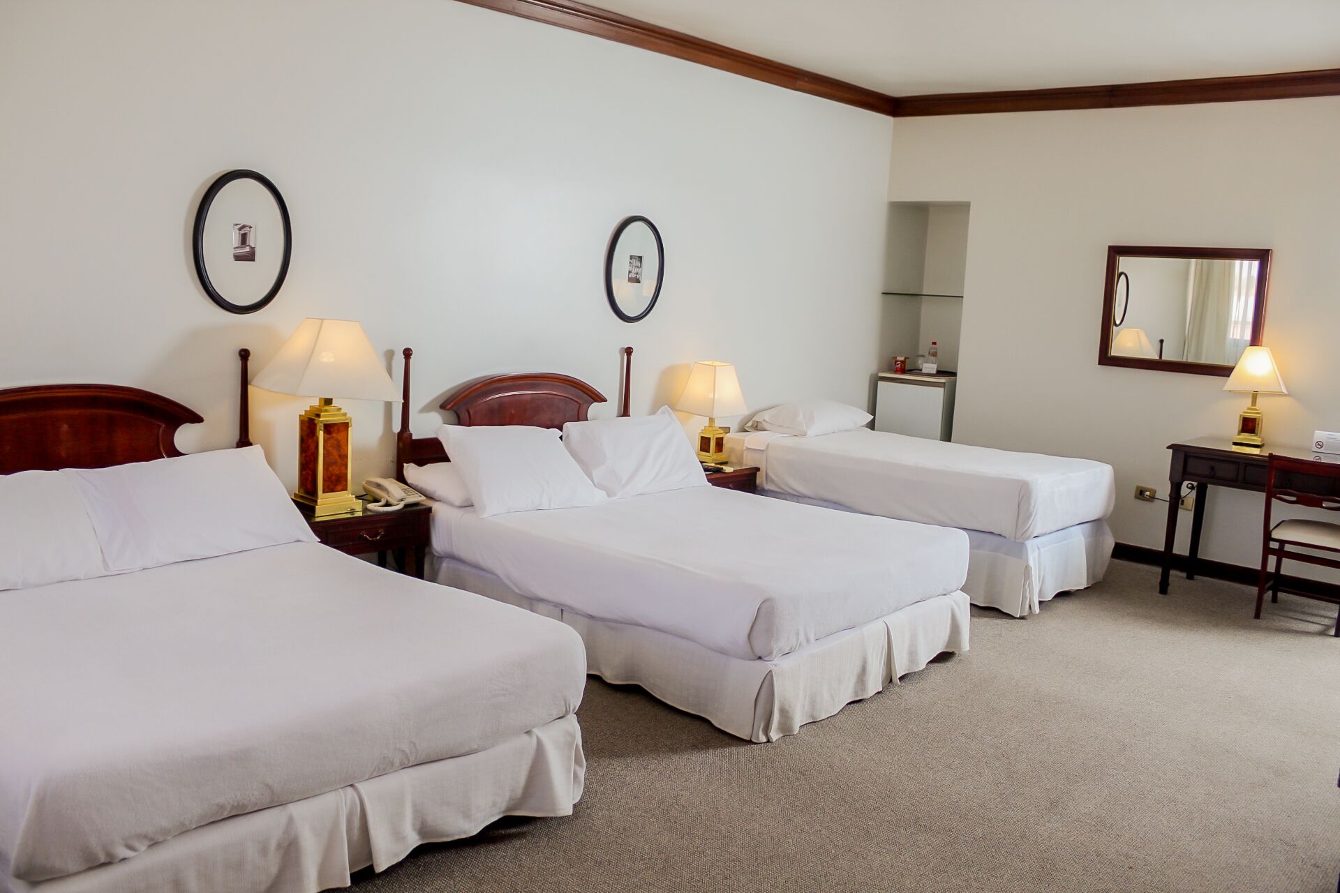 A hotel room with two single beds, a desk with a chair, a mirror, and two bedside lamps.