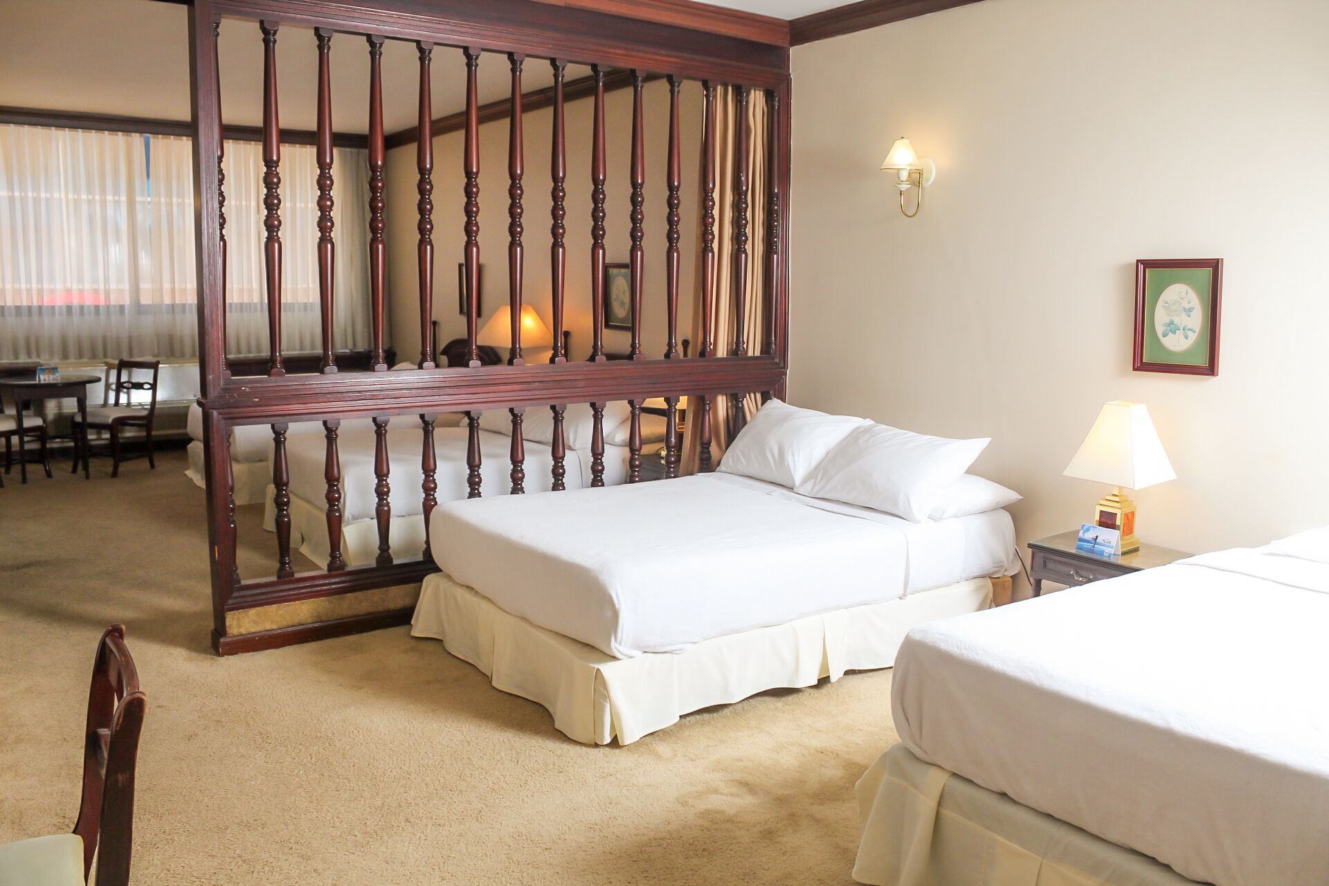A hotel room with a large bed, a smaller bed, a wooden partition, a desk, a chair, and a lamp.