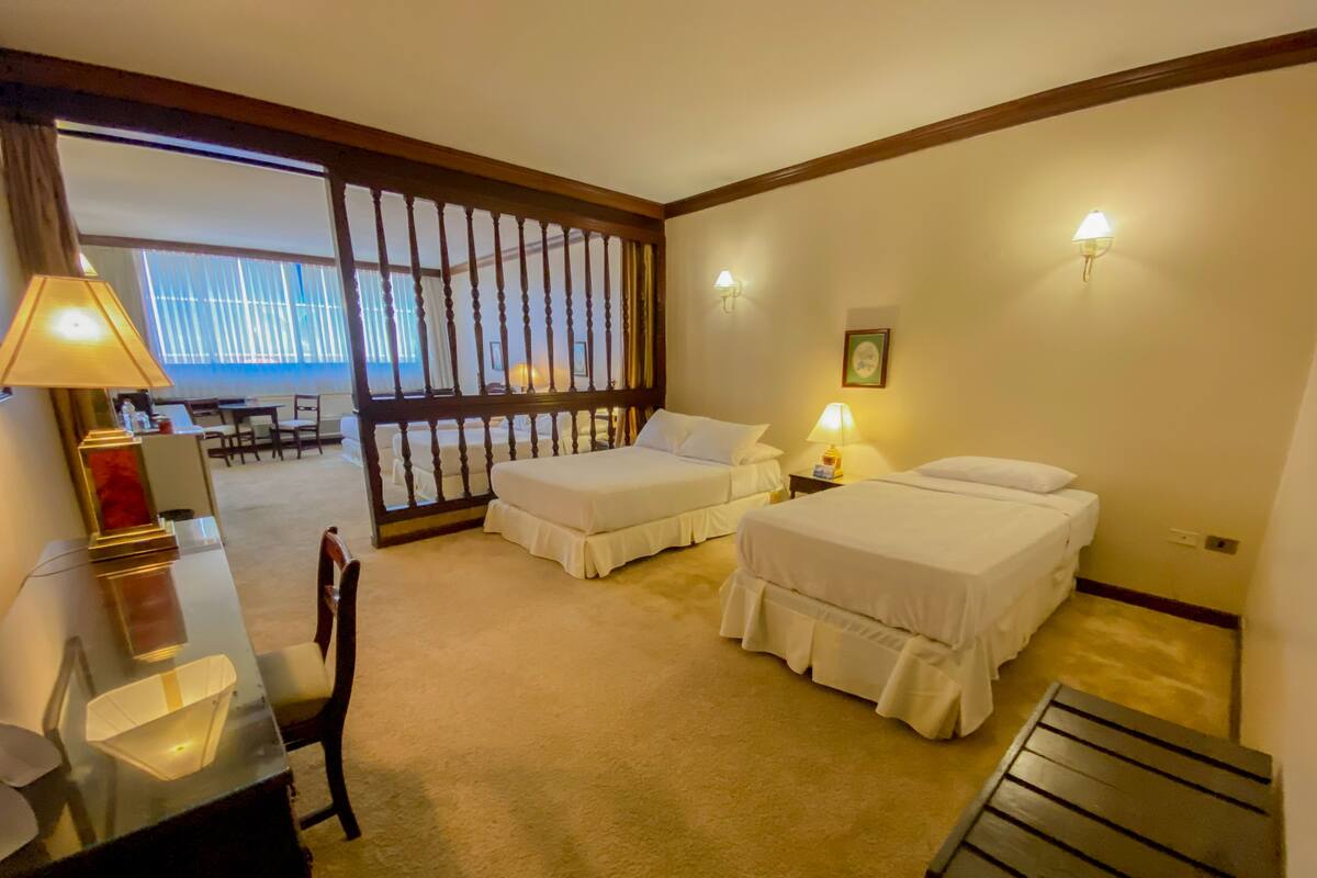 A hotel room with two beds, a desk, a chair, a lamp, and a view of the outside.