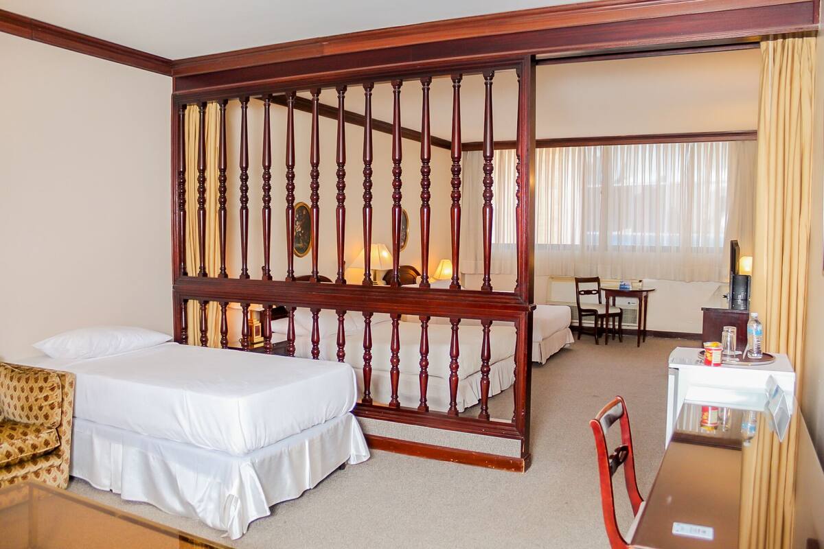A hotel room with a large bed, a sofa, a desk with a chair, and a TV.