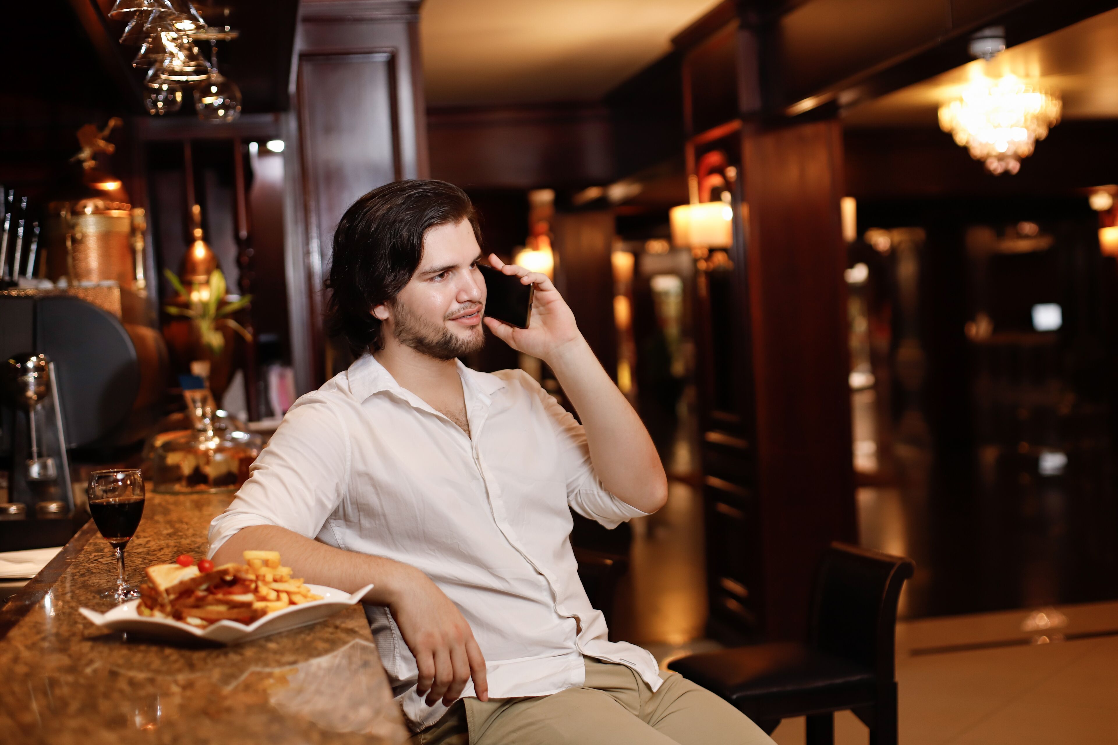 Un homme est assis au bar, devant une assiette de nourriture et un verre de vin rouge.
