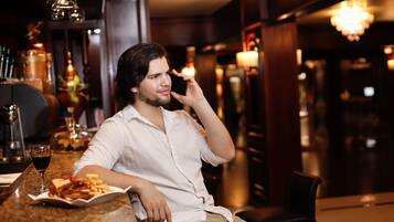 A man sitting at a bar with a plate of food and a glass of red wine.