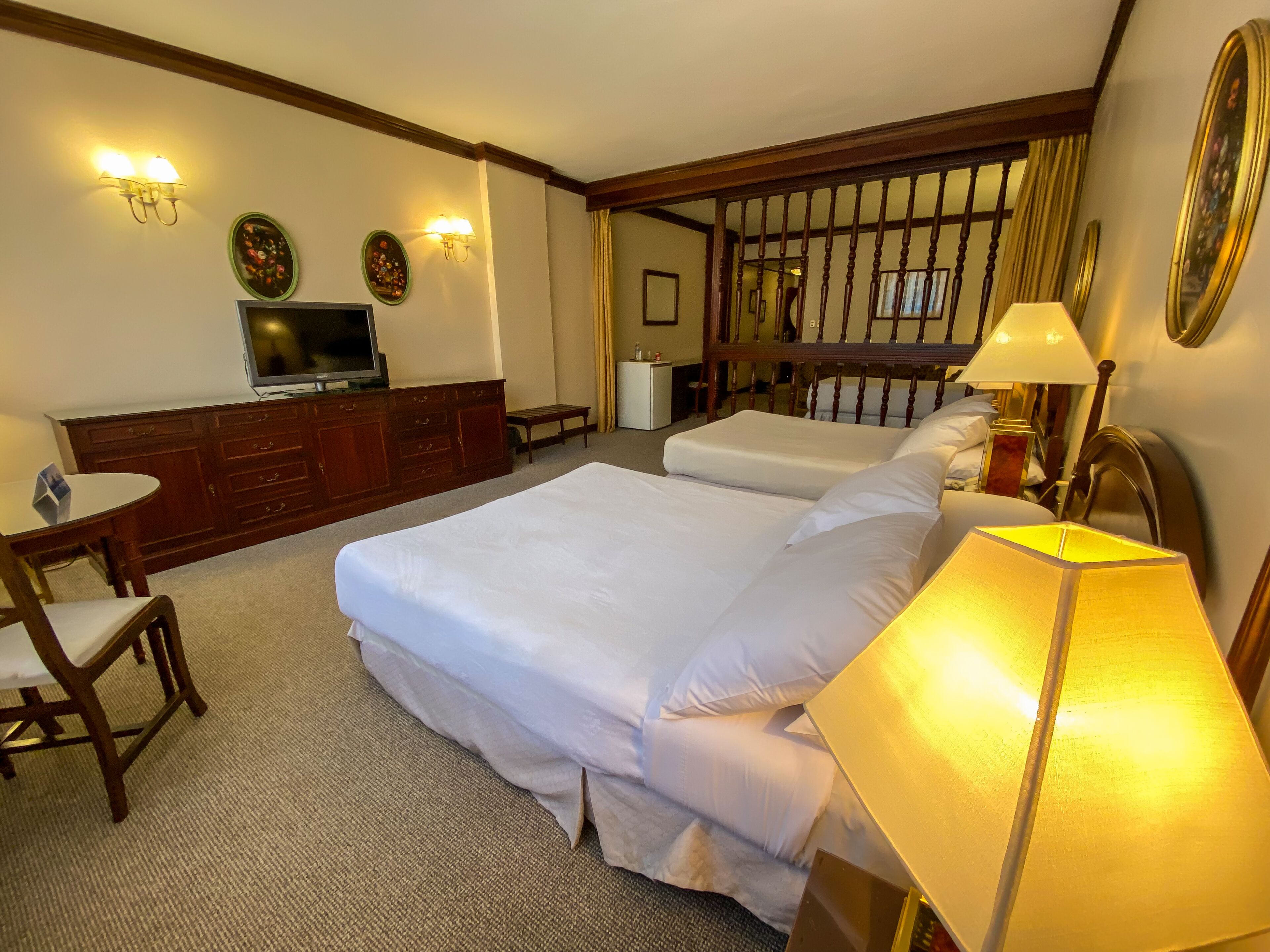 A hotel room with two beds, a desk, a television, and a lamp.