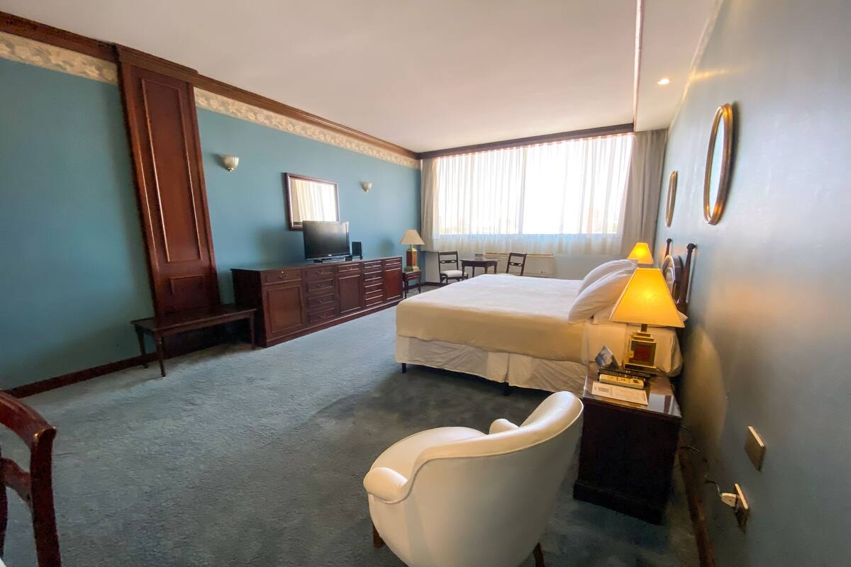 A hotel room with a bed, a desk, a chair, a television, and a lamp.