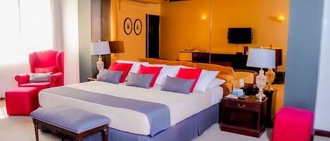 A hotel room with a large bed, a red armchair, a wooden nightstand, and a red ottoman.