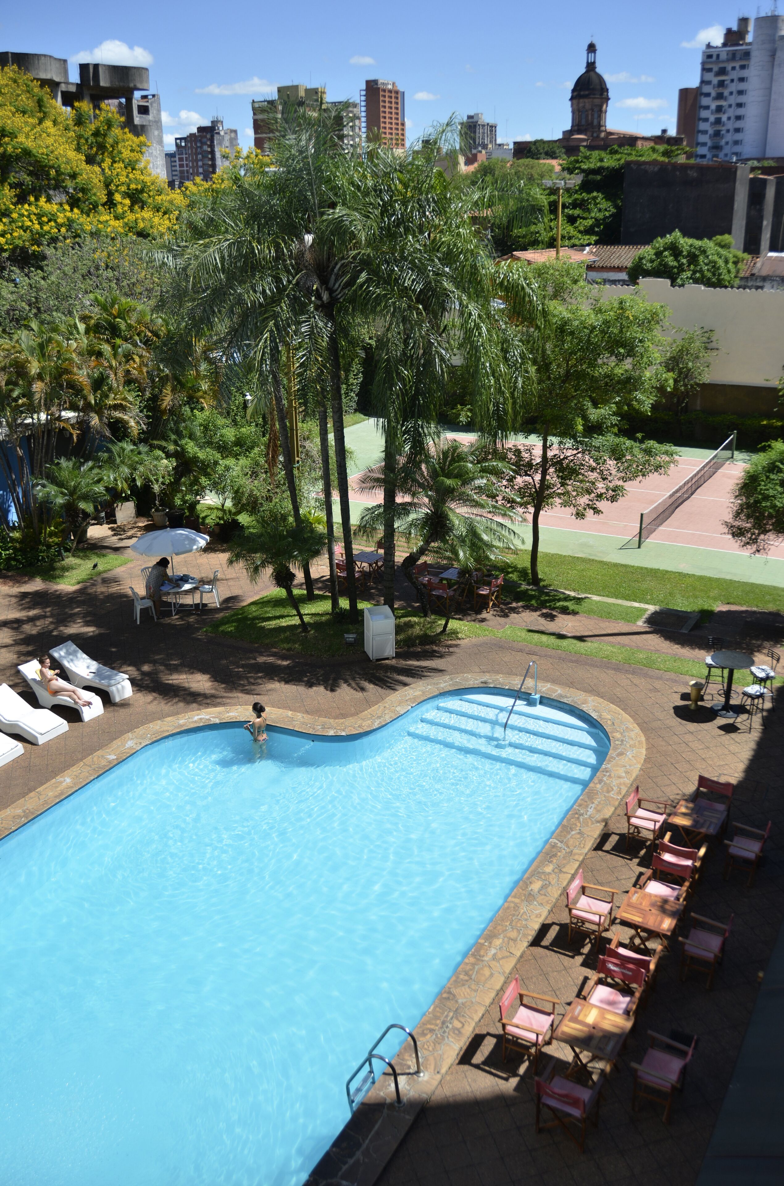A swimming pool with lounge chairs and a tennis court in the background.