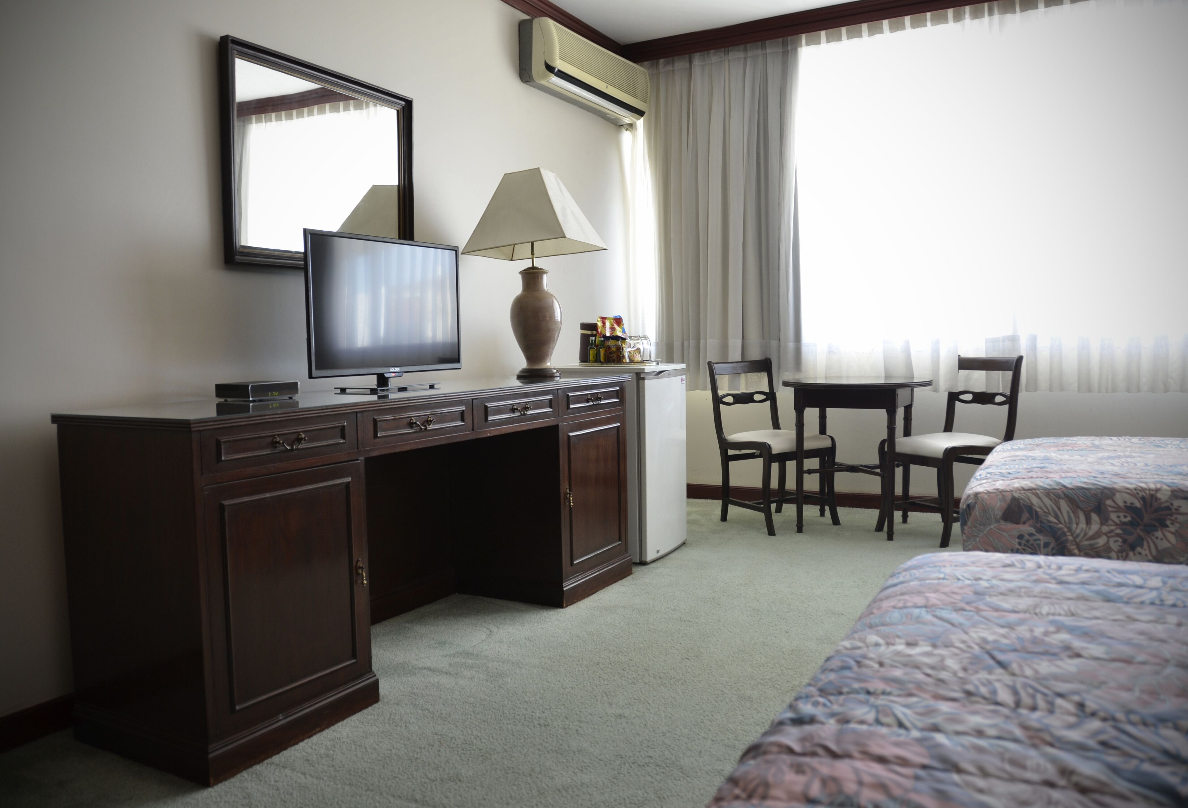 Een hotelkamer met een bureau, een televisie, een lamp, twee stoelen en een bed.