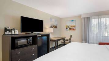 A hotel room with a bed, a desk, a television, a microwave, and a coffee maker.