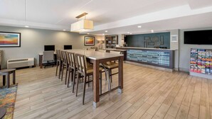 Un hall d’hôtel moderne avec une table à manger en bois, des chaises, un comptoir de réception et un grand écran de télévision.