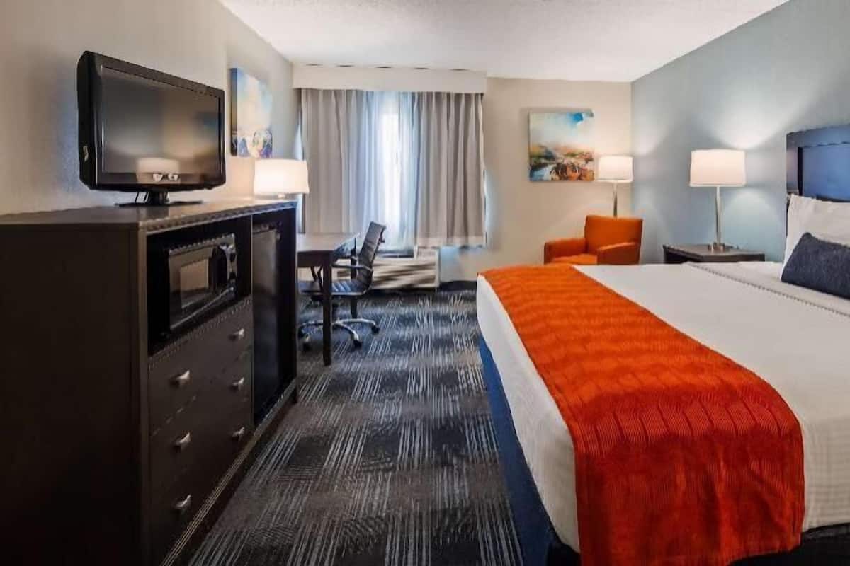 Een hotelkamer met een bed, een bureau, een stoel, een televisie en een schilderij aan de muur.