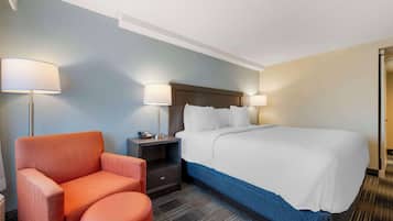Une chambre d’hôtel avec un grand lit, deux lampes de chevet, une table de chevet, un fauteuil rouge et un petit pouf.