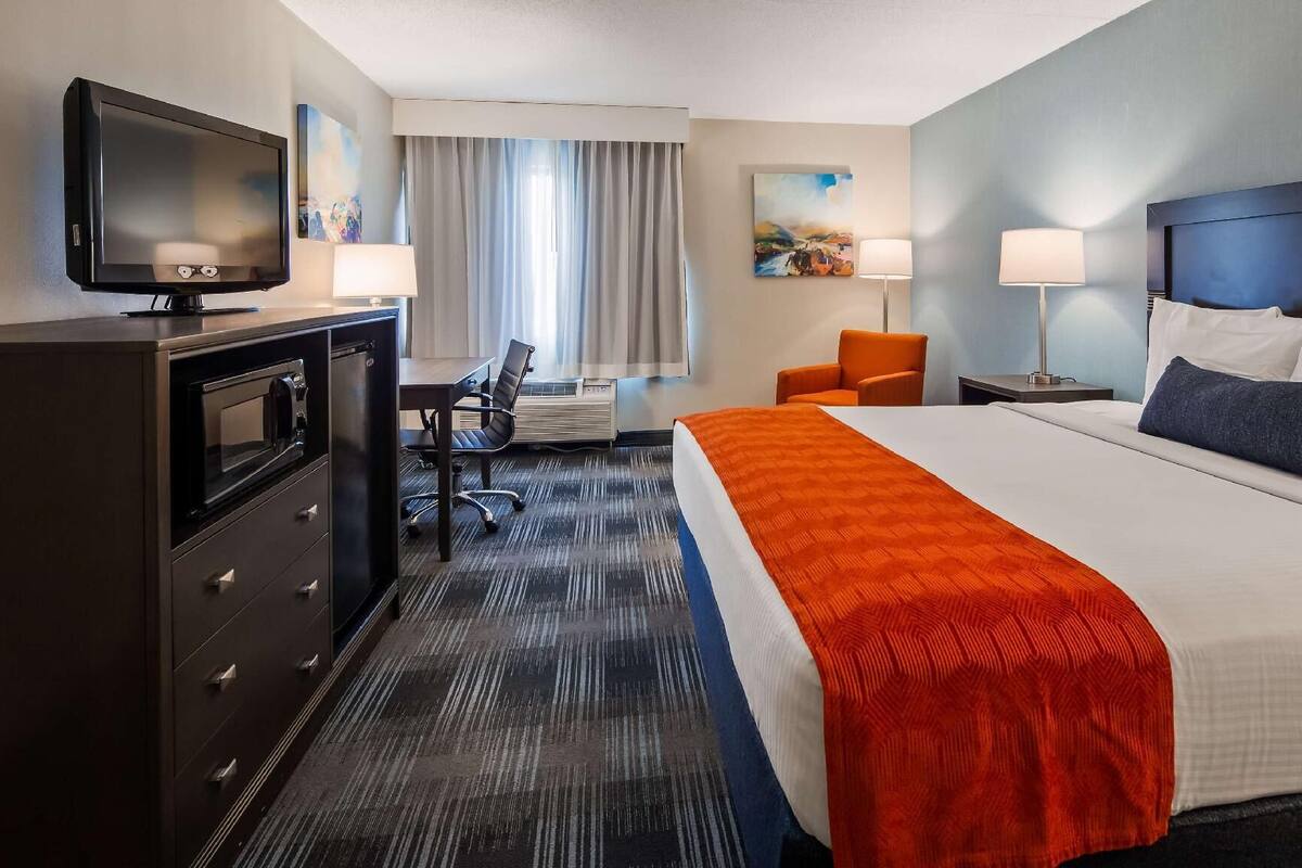 Een hotelkamer met een bed, een bureau, een stoel, een televisie en een schilderij aan de muur.