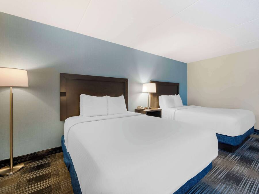 Una habitación de hotel con dos camas, una mesita de noche con lámpara y piso alfombrado.