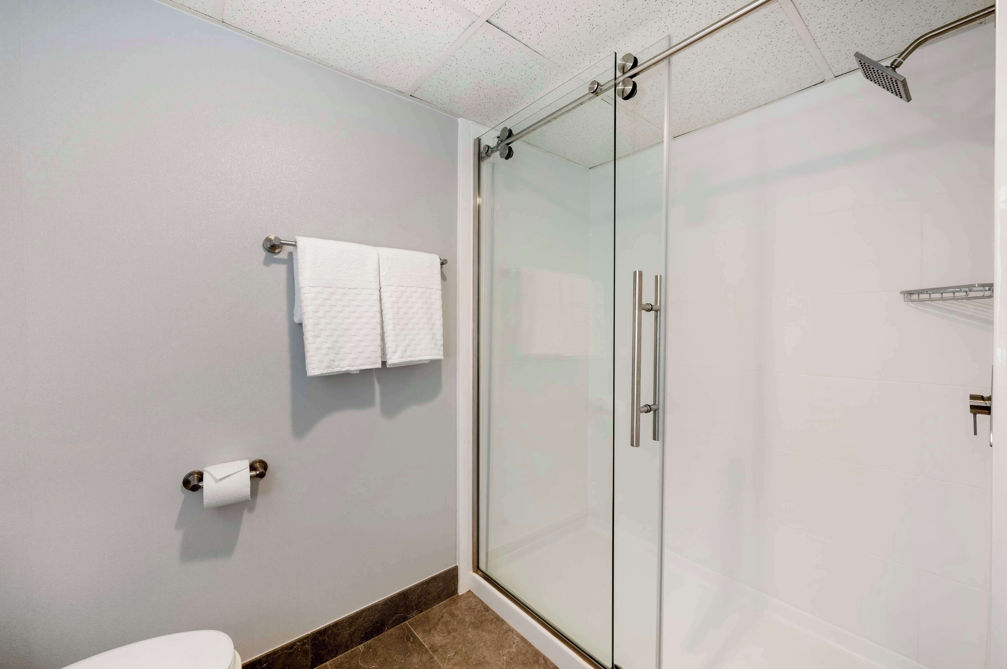 A modern bathroom with a glass shower enclosure, a toilet, and a towel rack with multiple towels.