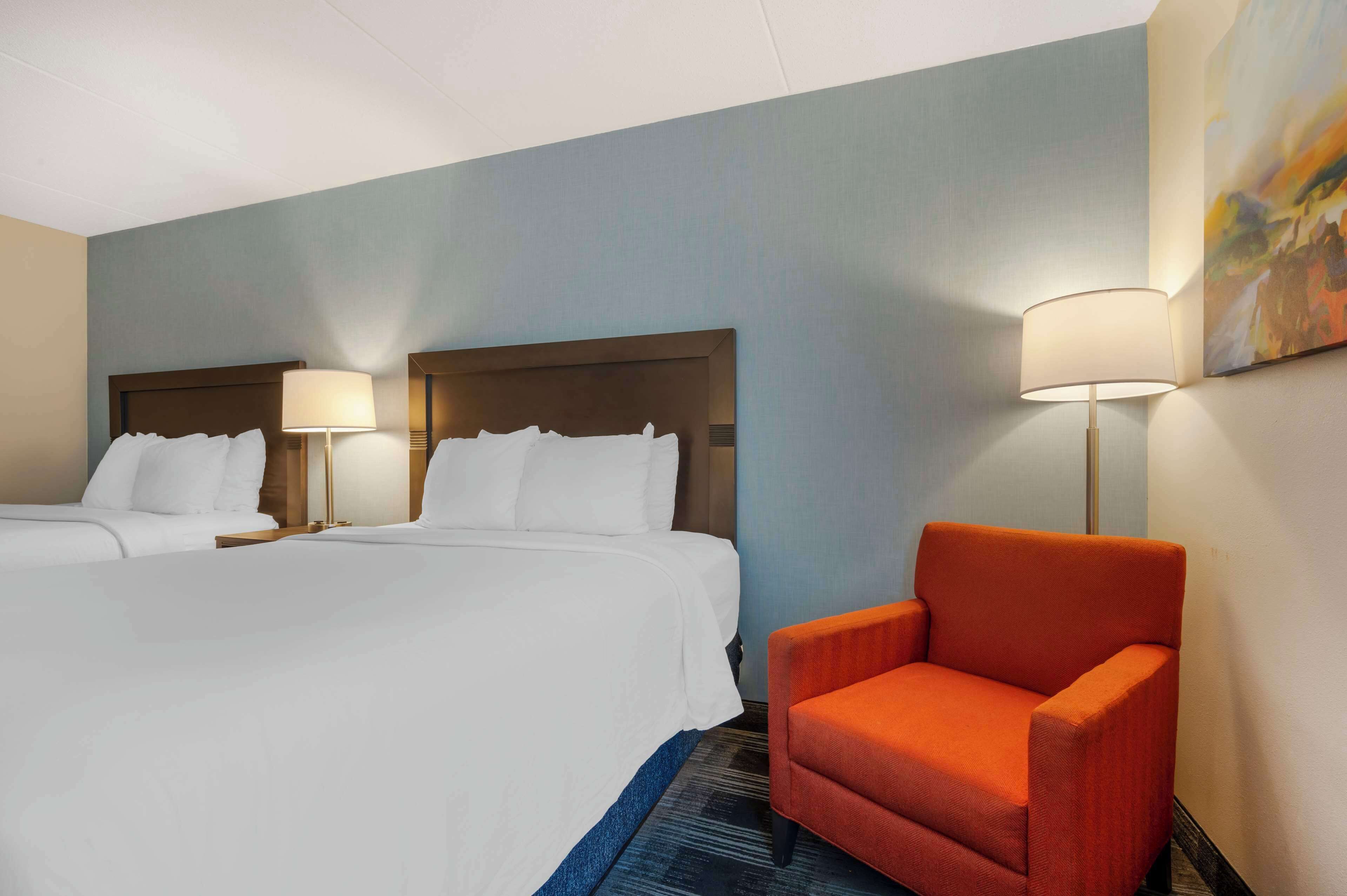 A hotel room with two beds, a red armchair, and a painting on the wall.