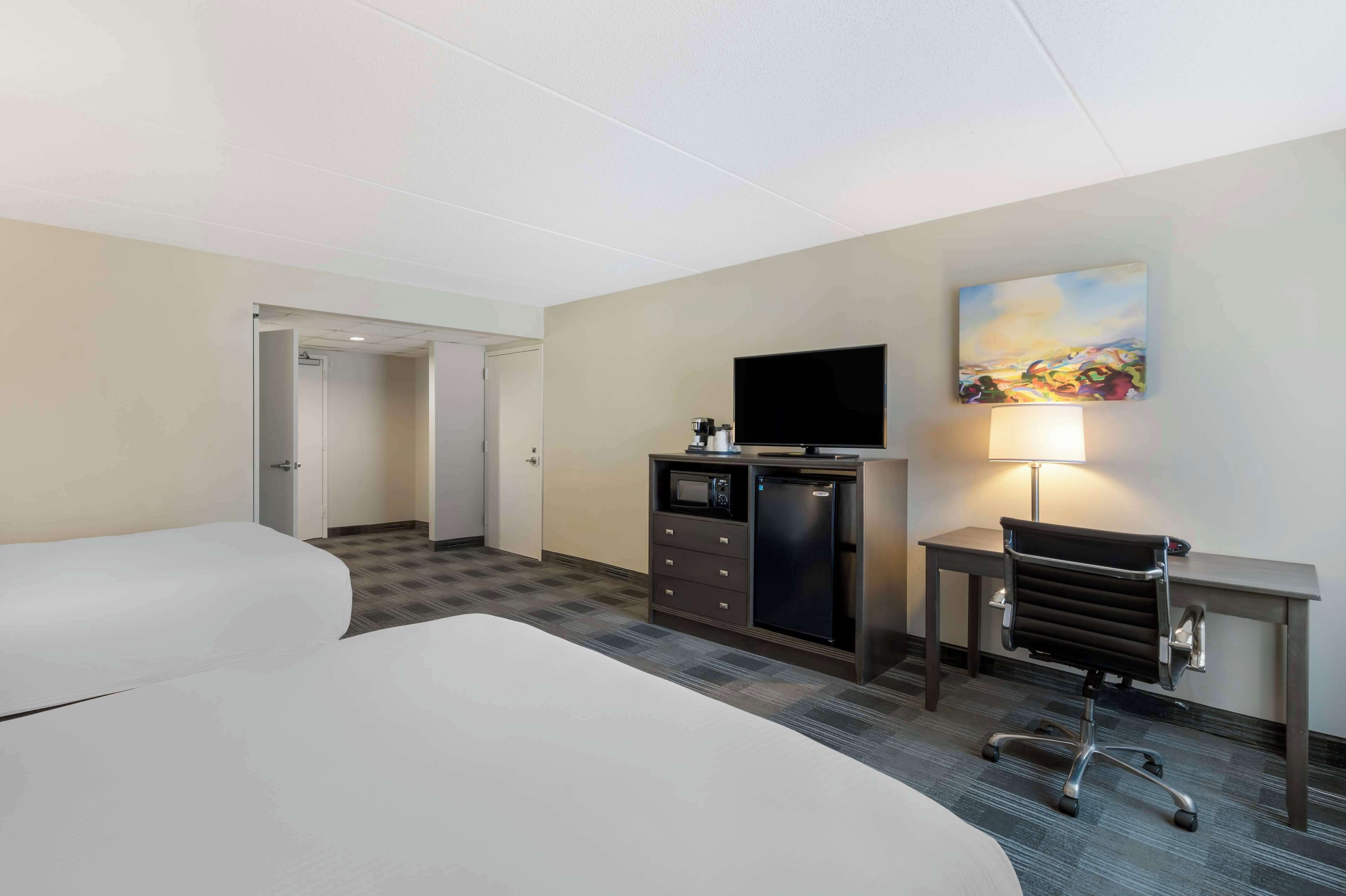 Habitación de hotel con cama, escritorio con computadora, televisión y un cuadro en la pared.