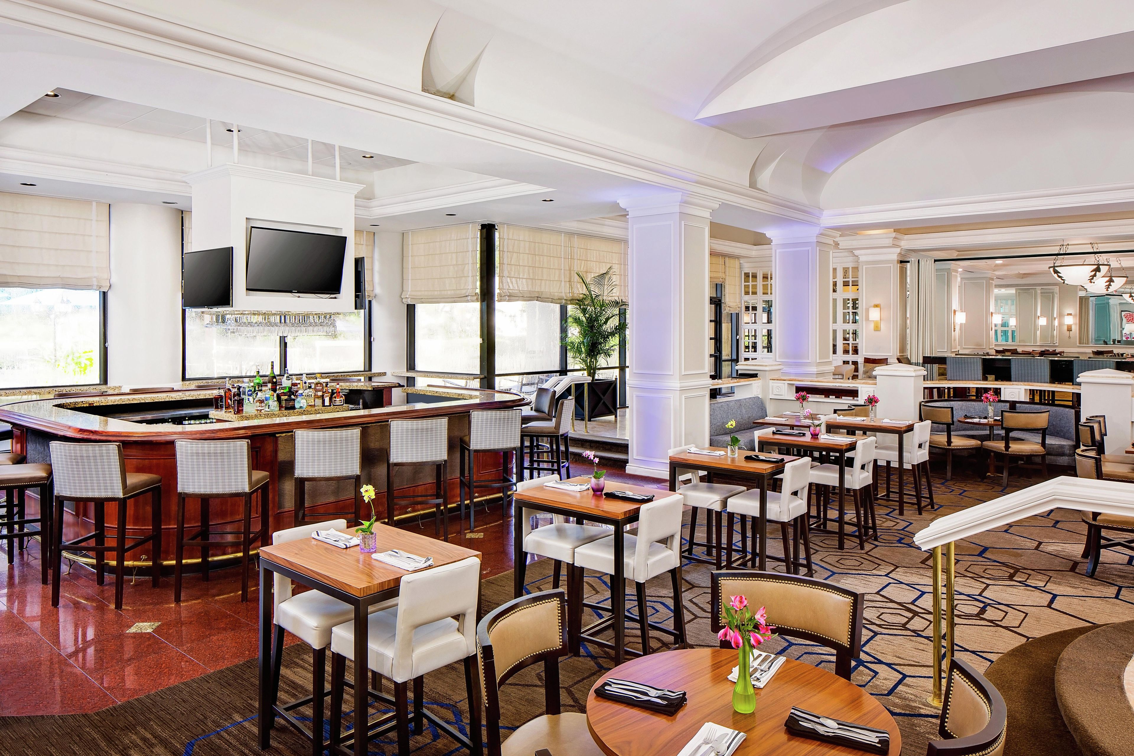 Un vestíbulo de hotel con zona de bar, espacios de descanso y un televisor.