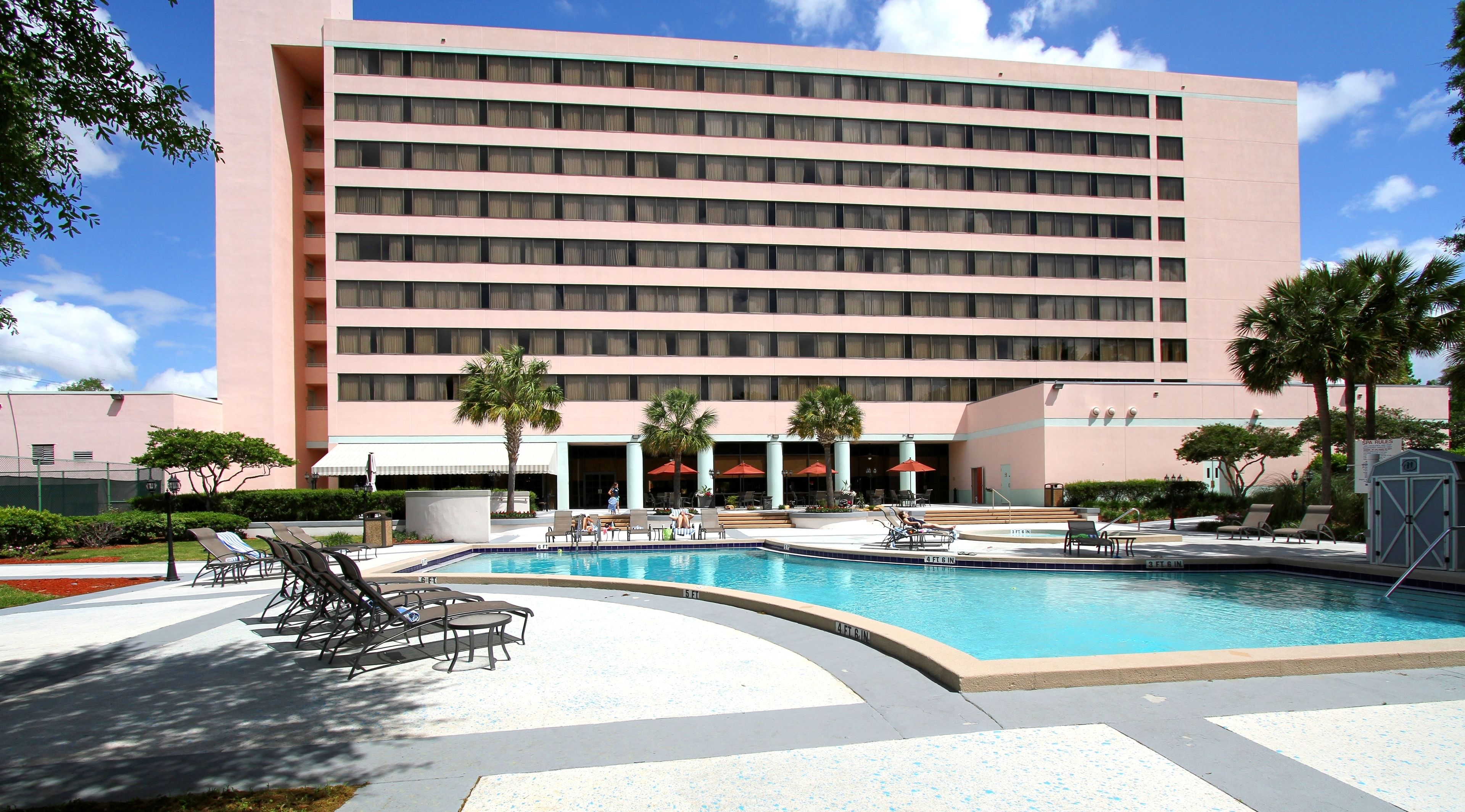 A hotel with a swimming pool, sun loungers, and palm trees.