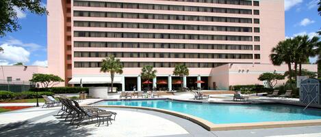 A hotel with a swimming pool, sun loungers, and palm trees.