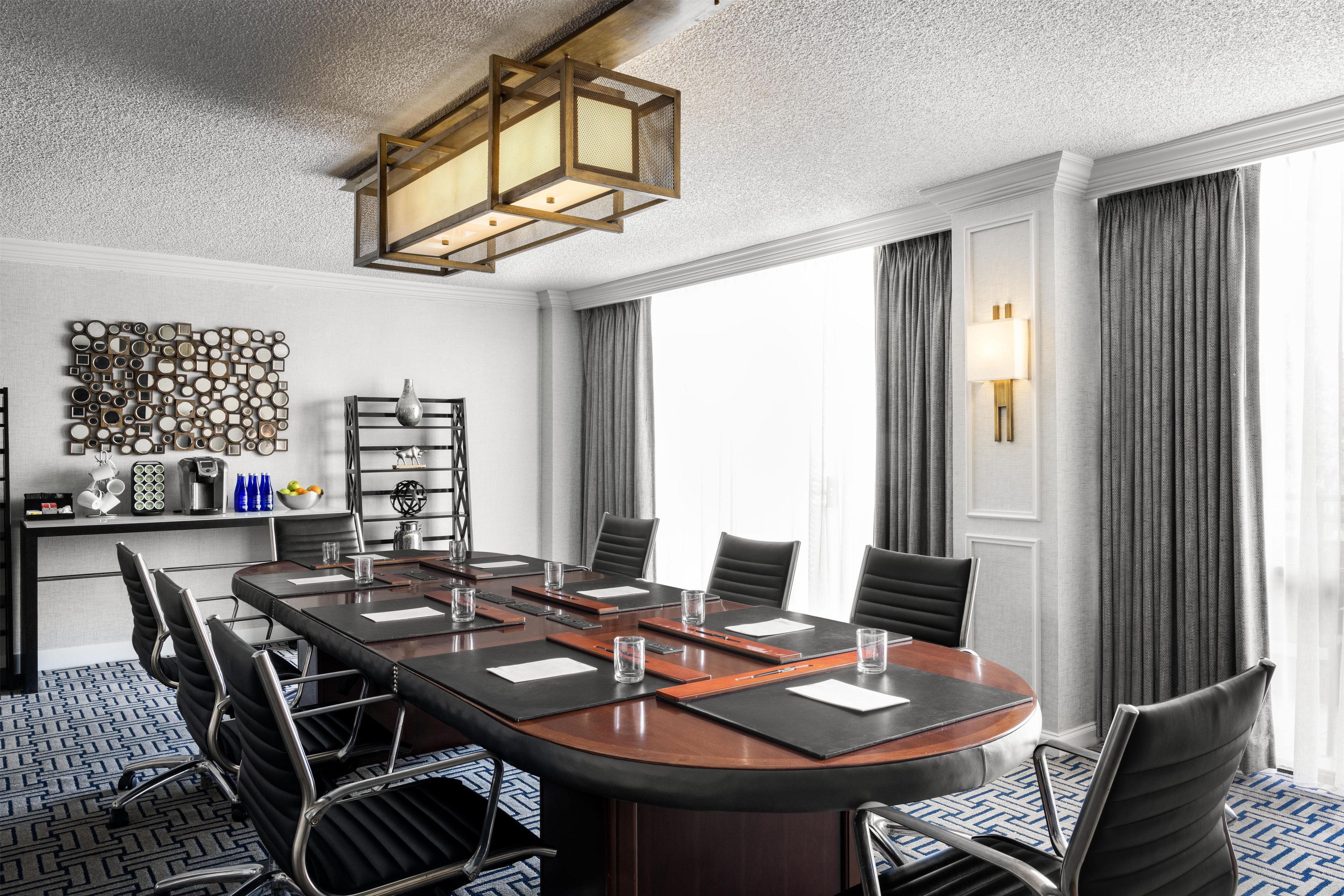 A conference room with a large oval table, black chairs, a coffee station, and a decorative wall piece.