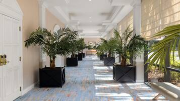A corridor with a patterned floor, potted plants, and a bench.