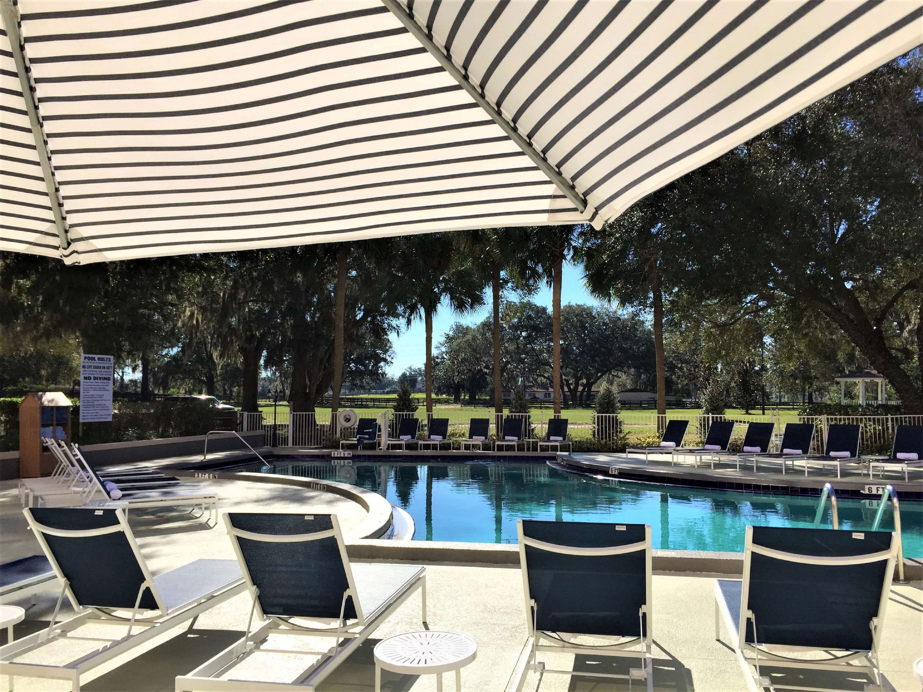 Un espace aménagé au bord de la piscine, avec des chaises longues et des parasols, une piscine, et un panneau indiquant les règles à respecter.