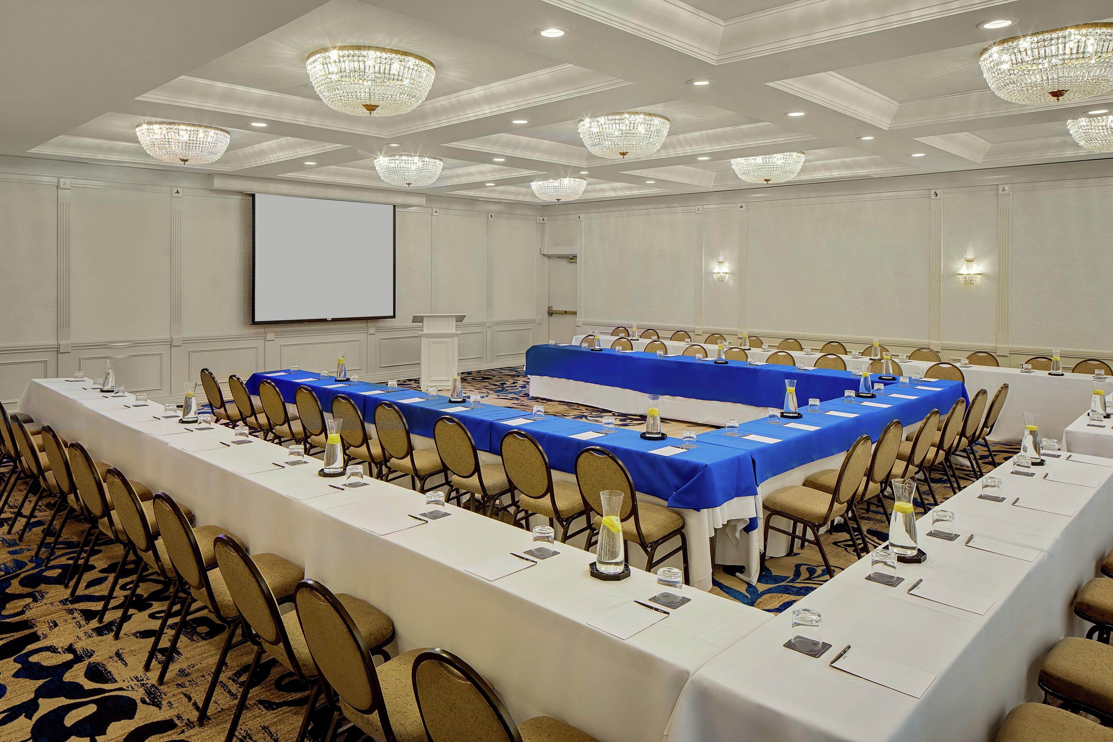 A conference room with long tables, chairs, and a projector screen.