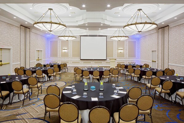 Un salón de conferencias con varias mesas y sillas, una pantalla grande y candelabros.