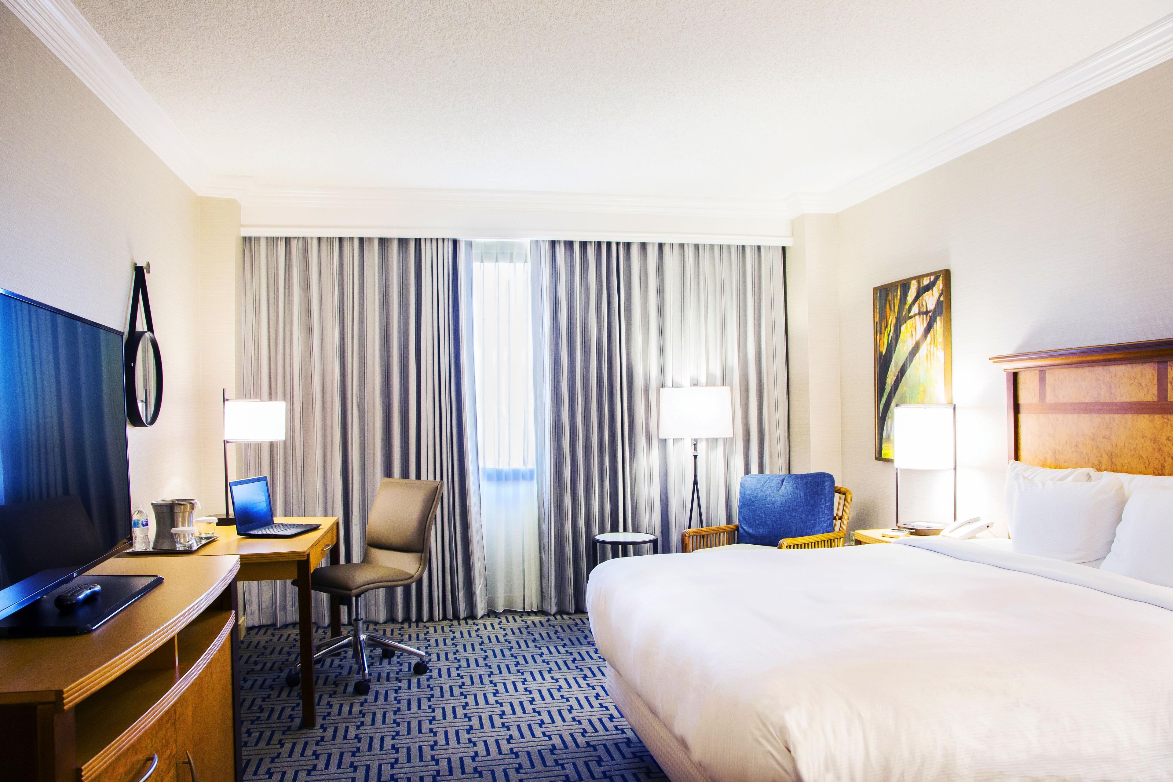 A hotel room with a bed, desk, chair, television, and curtains.