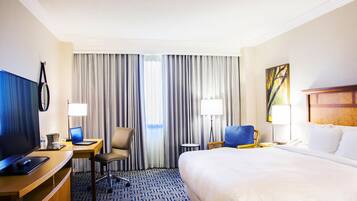 A hotel room with a bed, desk, chair, television, and curtains.