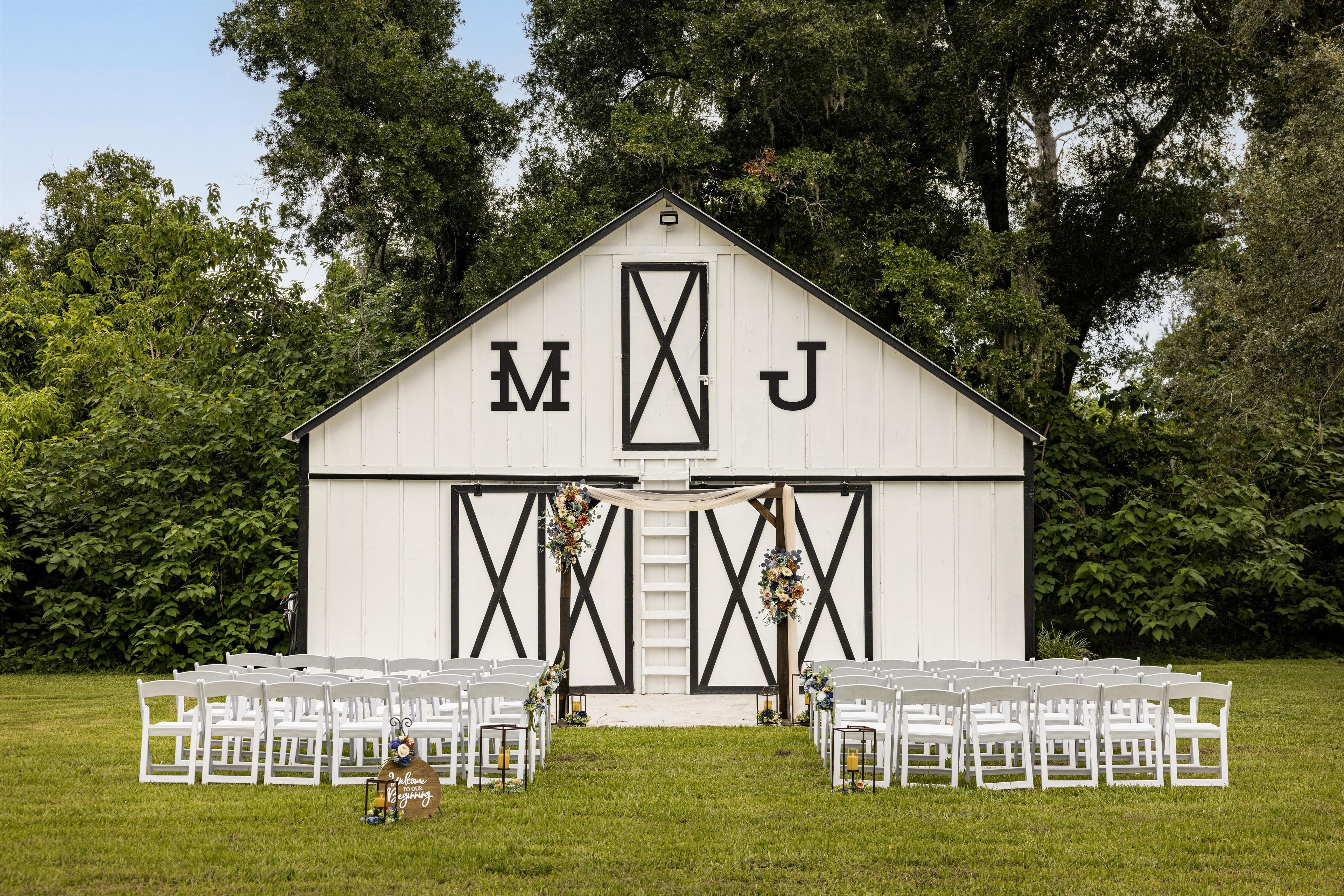 A white barn-style building with 'MJ' on the front, surrounded by white chairs arranged in rows.