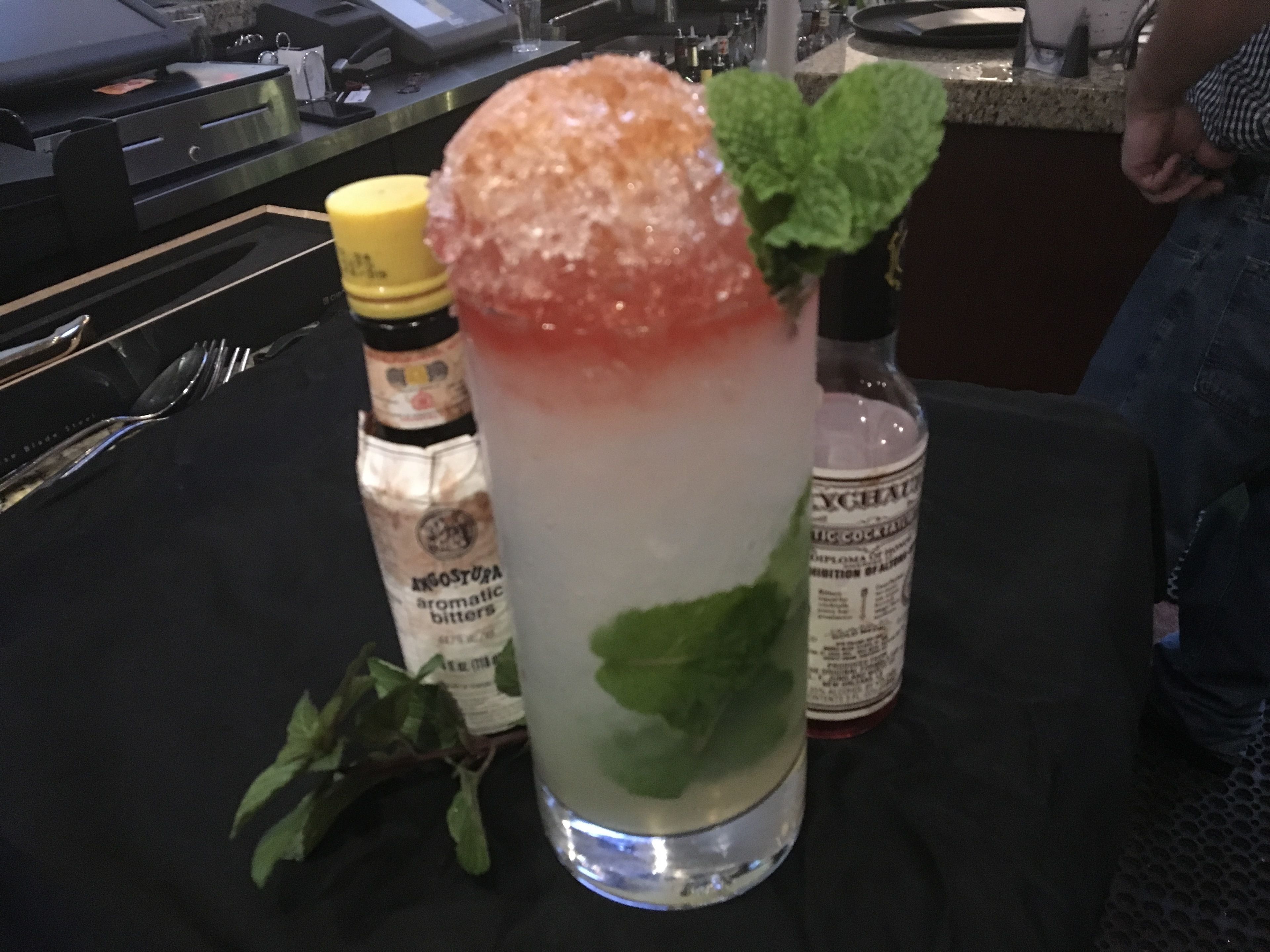A cocktail with a salted rim and mint garnish on a bar counter.