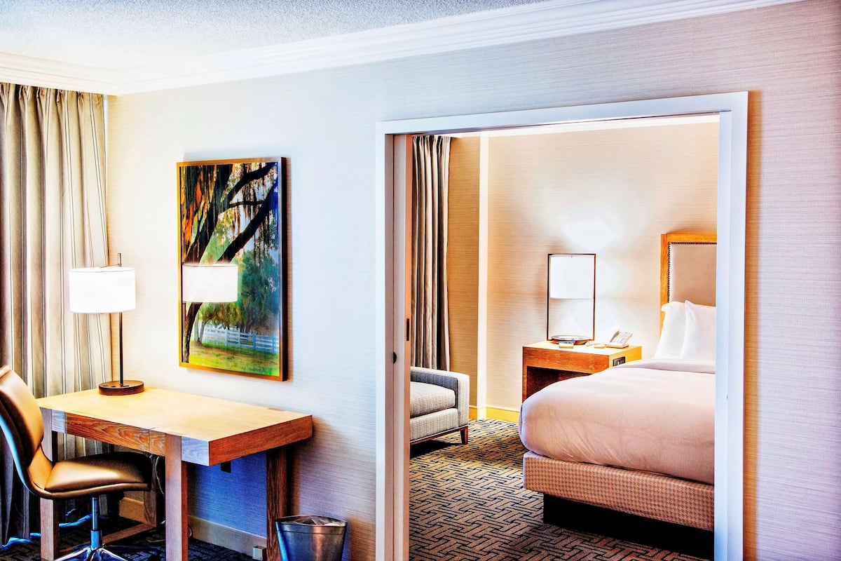 A hotel room with a desk, chair, bed, and a painting on the wall.