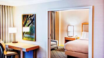 Quarto de hotel com escrivaninha, cadeira, cama e um quadro na parede.